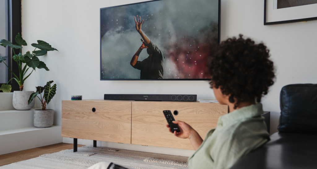 Person bedient Fernseher, auf dem Sideboard eine Cinebar 11